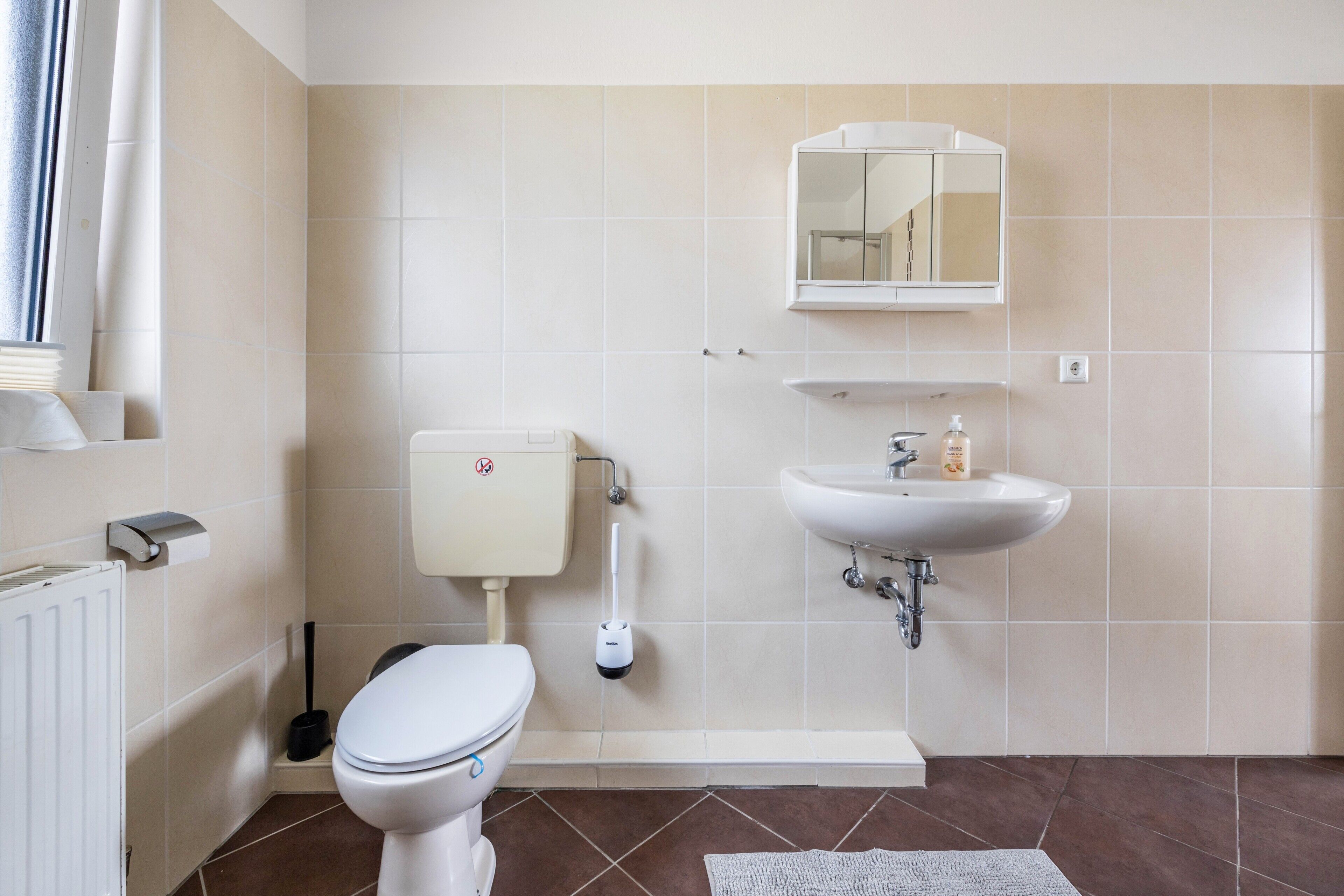 A bathroom with a toilet, bidet, sink, mirror, and a window with a curtain.