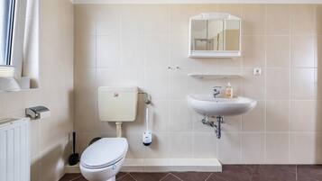 A bathroom with a toilet, bidet, sink, mirror, and a window with a curtain.