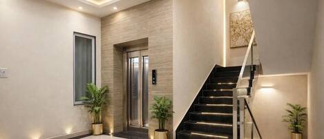 A modern interior with a staircase, elevator, and potted plants.