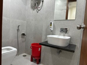 Une salle de bain avec un lavabo blanc, des toilettes, une douche et un seau rouge.