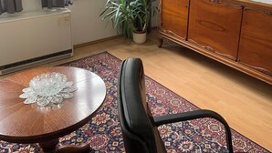 A room with a wooden cabinet, a television, a potted plant, a patterned rug, and a round table with a glass centerpiece. - HGALTSTADTFEWO (Wismar)