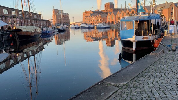 A calm harbor with boats docked, a cobblestone waterfront, and buildings in the background. - HGALTSTADTFEWO (Wismar)
