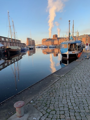 Ein ruhiger Hafen mit vertäuten Booten, einer Kopfsteinpflasterpromenade und Gebäuden im Hintergrund.