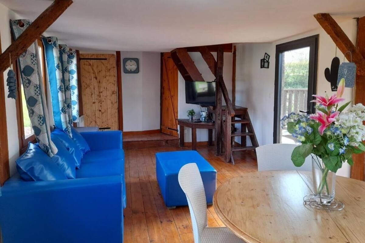Una sala de estar acogedora con un sofá azul, una mesa de comedor de madera y un televisor al fondo.