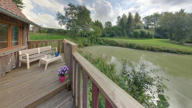 A wooden deck with a bench and table, overlooking a river and greenery. - Holiday Village (Reclinghem)