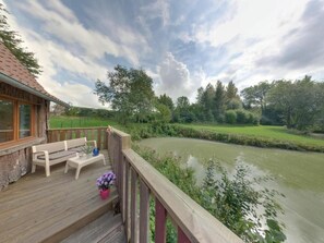 Terraza de madera con banco y mesa, con vistas a un río y vegetación.