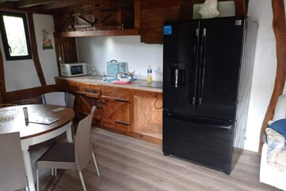 A kitchen with wooden cabinets, a black refrigerator, a microwave, and a dining table with chairs.
