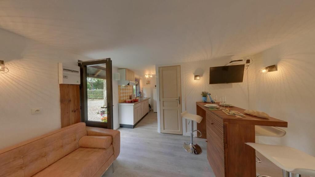 A compact living space with a sofa, a wooden bar area, a kitchen, and a TV mounted on the wall.