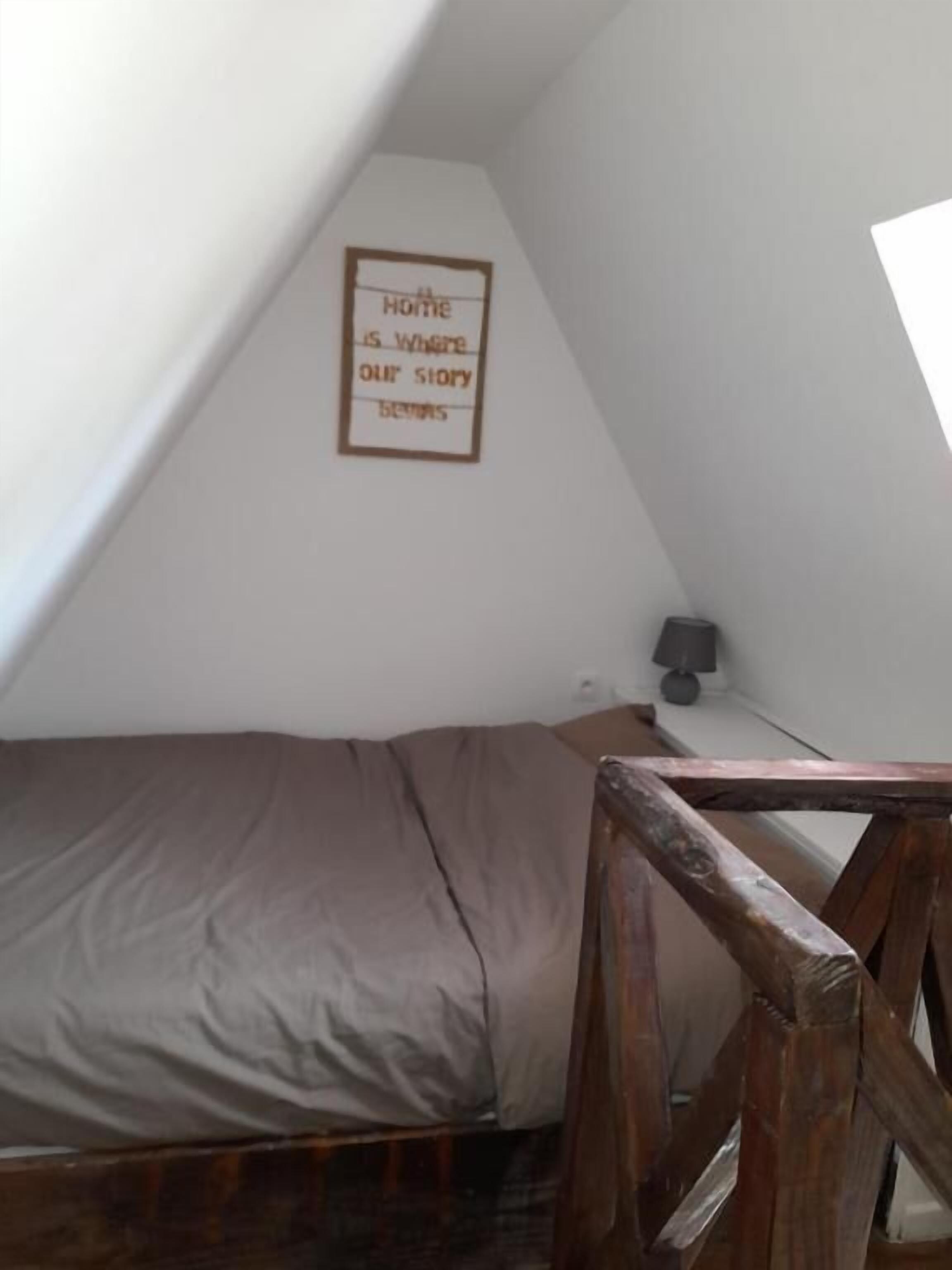 A small, sloped-roofed room with a single bed, a wooden bench, and a framed quote on the wall.