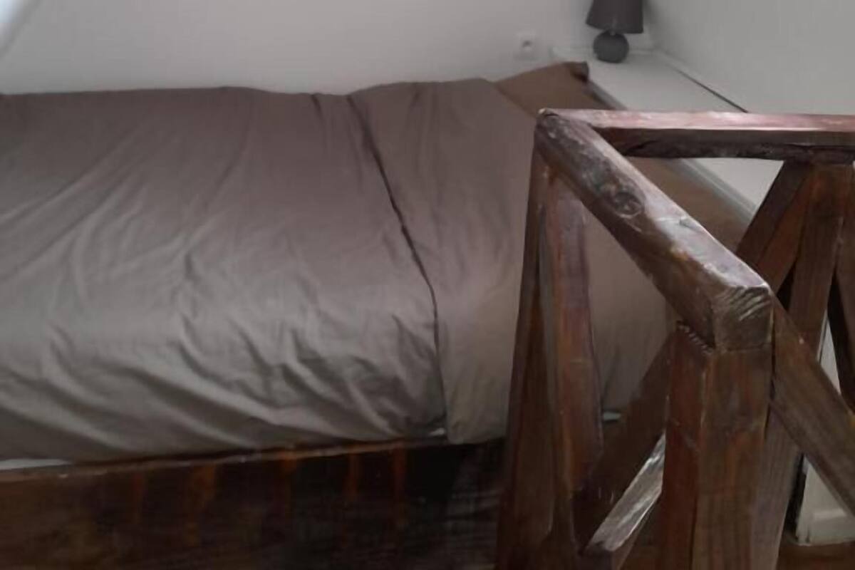 Una habitación pequeña con techo inclinado, una cama individual, un banco de madera y una cita en un marco en la pared.