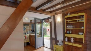 A rustic kitchen with wooden beams, a yellow cabinet, and a sliding glass door leading to an outdoor area. - Holiday Village (Reclinghem)