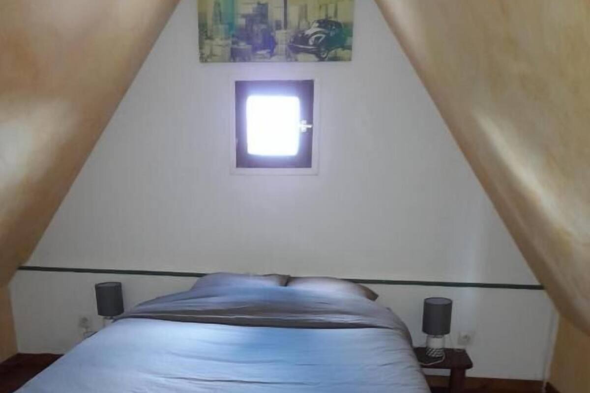 Un dormitorio con una cama individual, un ventanal pequeño y dos mesitas de noche con lámparas.