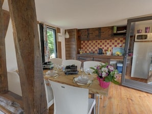 A rustic kitchen with wooden cabinets, a checkered backsplash, and a dining table set for two with white chairs. - Holiday Village (Reclinghem)