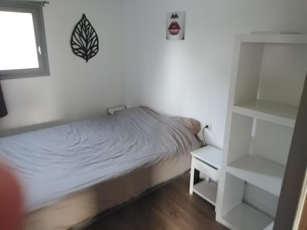 A bedroom with a single bed, a nightstand, a wall decoration, and a white shelving unit.