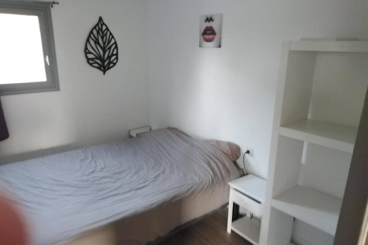 A bedroom with a single bed, a nightstand, a wall decoration, and a white shelving unit.