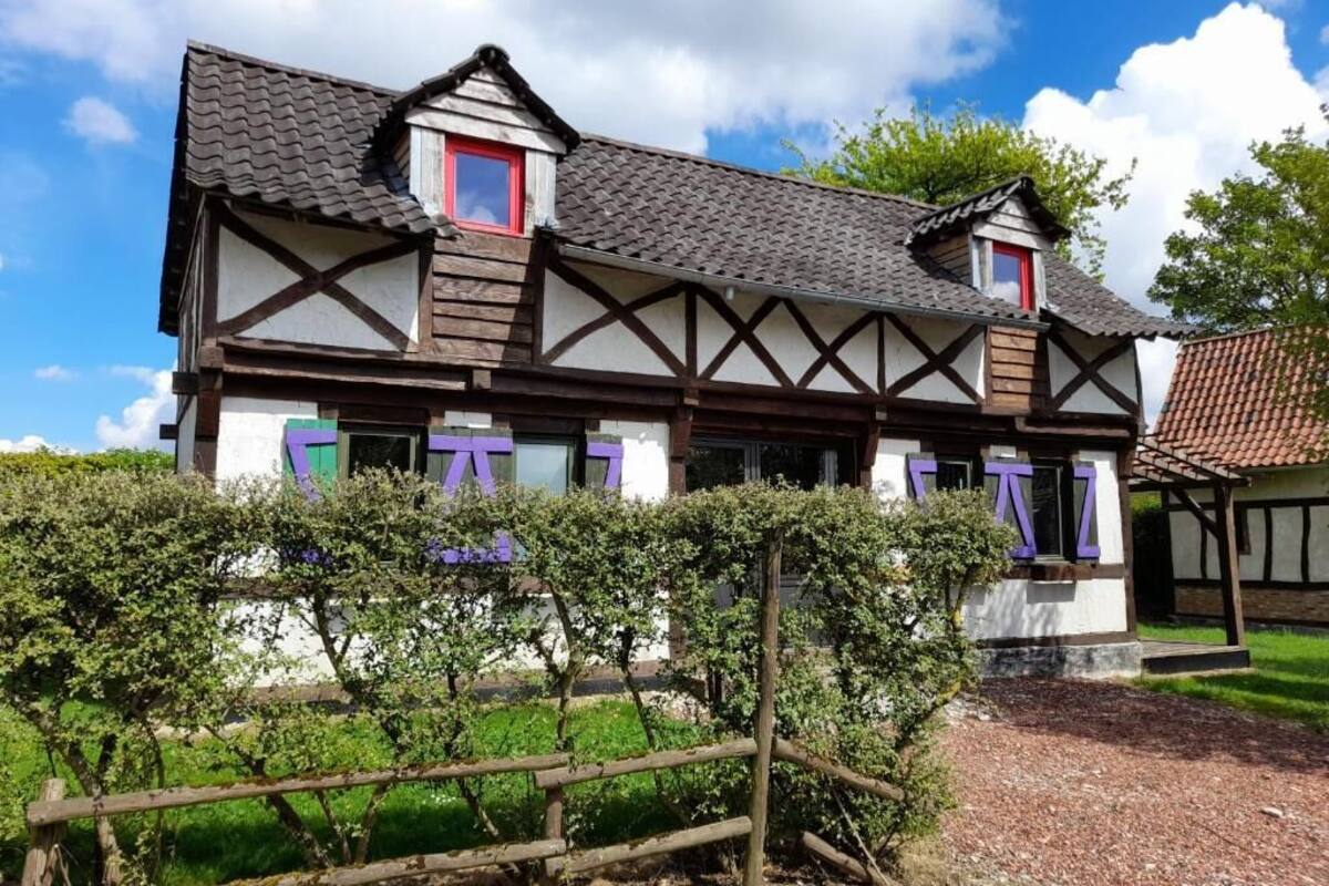 Una casa tradicional de entramado con tejado inclinado, varias ventanas con contraventanas y un pequeño jardín con valla de madera.