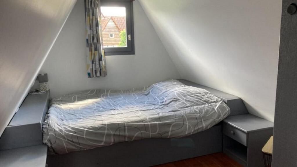 A small, sloped ceiling room with a single bed, a window, and a view of a house outside.