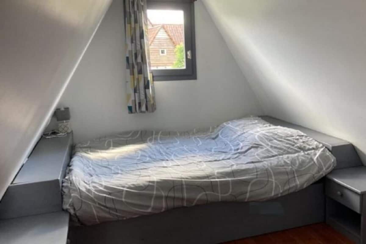 A small, sloped ceiling room with a single bed, a window, and a view of a house outside.