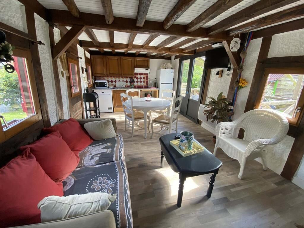 A cozy interior with a sofa, dining table, and chairs, wooden beams on the ceiling, and a view of the outdoors.