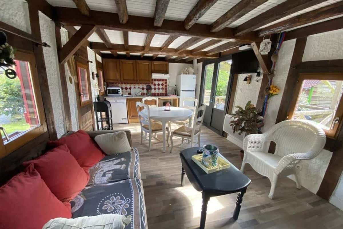 A cozy interior with a sofa, dining table, and chairs, wooden beams on the ceiling, and a view of the outdoors.