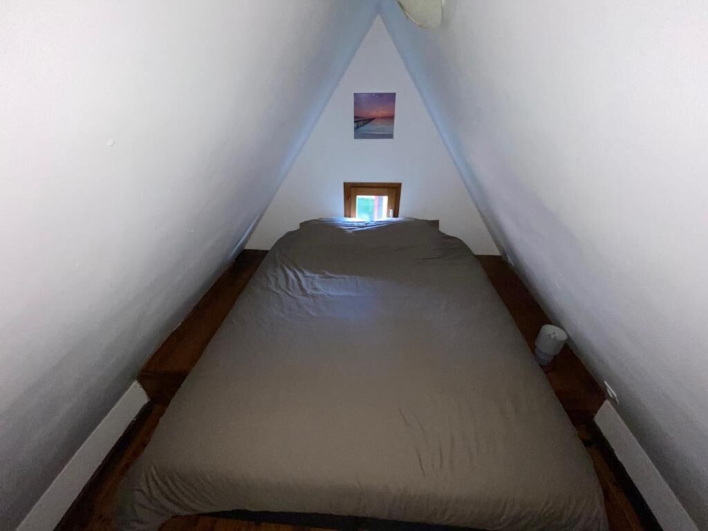 A narrow, triangular attic bedroom with a bed, a small window, and a picture on the wall.