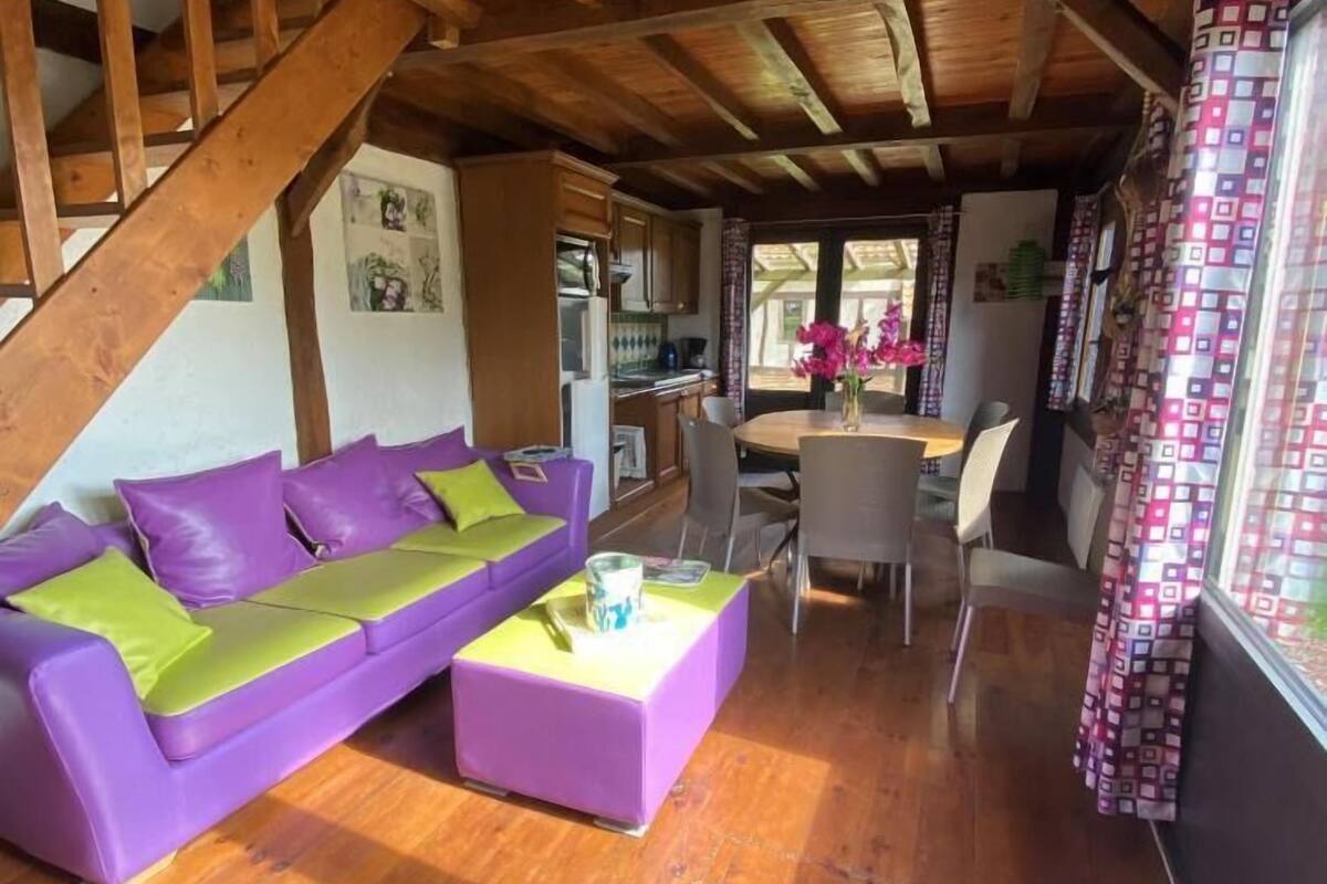 Un salón acogedor con techo de madera, un sofá morado, una mesita de centro y un comedor con sillas y una mesa.