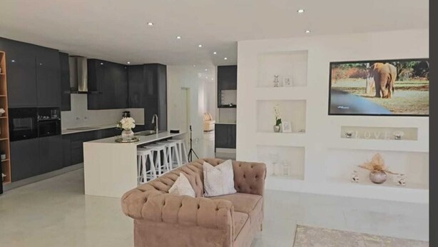 A modern living room with a sofa, a TV mounted on the wall, and a kitchen area in the background. - The View Luxury Guest House (Chinhoyi)
