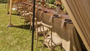 A tented outdoor dining area with tables set for a meal, surrounded by greenery and a stone wall. - The View Luxury Guest House (Chinhoyi)