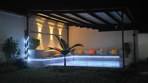 A modern outdoor seating area with a curved bench, ambient lighting, and a pergola structure. - The View Luxury Guest House (Chinhoyi)