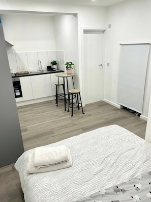 Una habitación compacta con cama, kitchenette y un armario blanco.