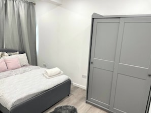 Un dormitorio con cama, armario gris y cortina gris.