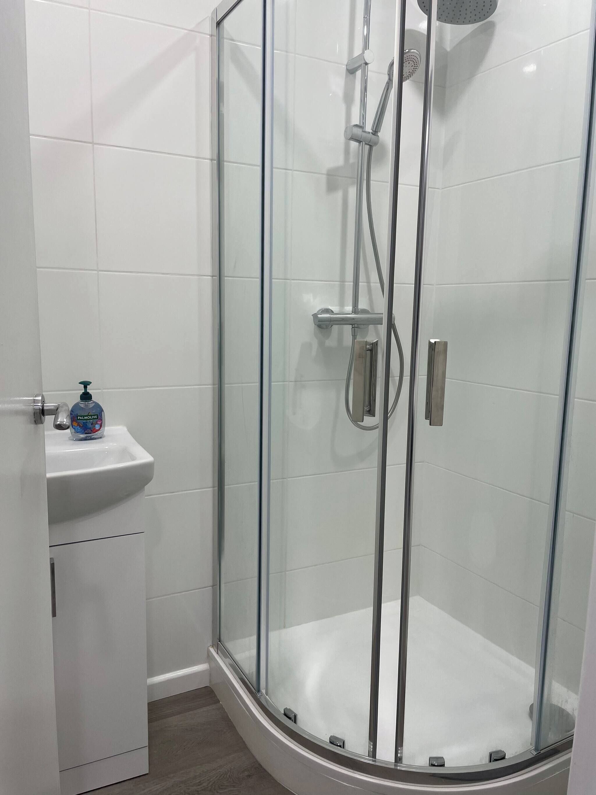 Ein modernes Badezimmer mit einer Glastrennwand-Dusche, einem weißen Waschbecken und einer Flasche Palmolive Seife.
