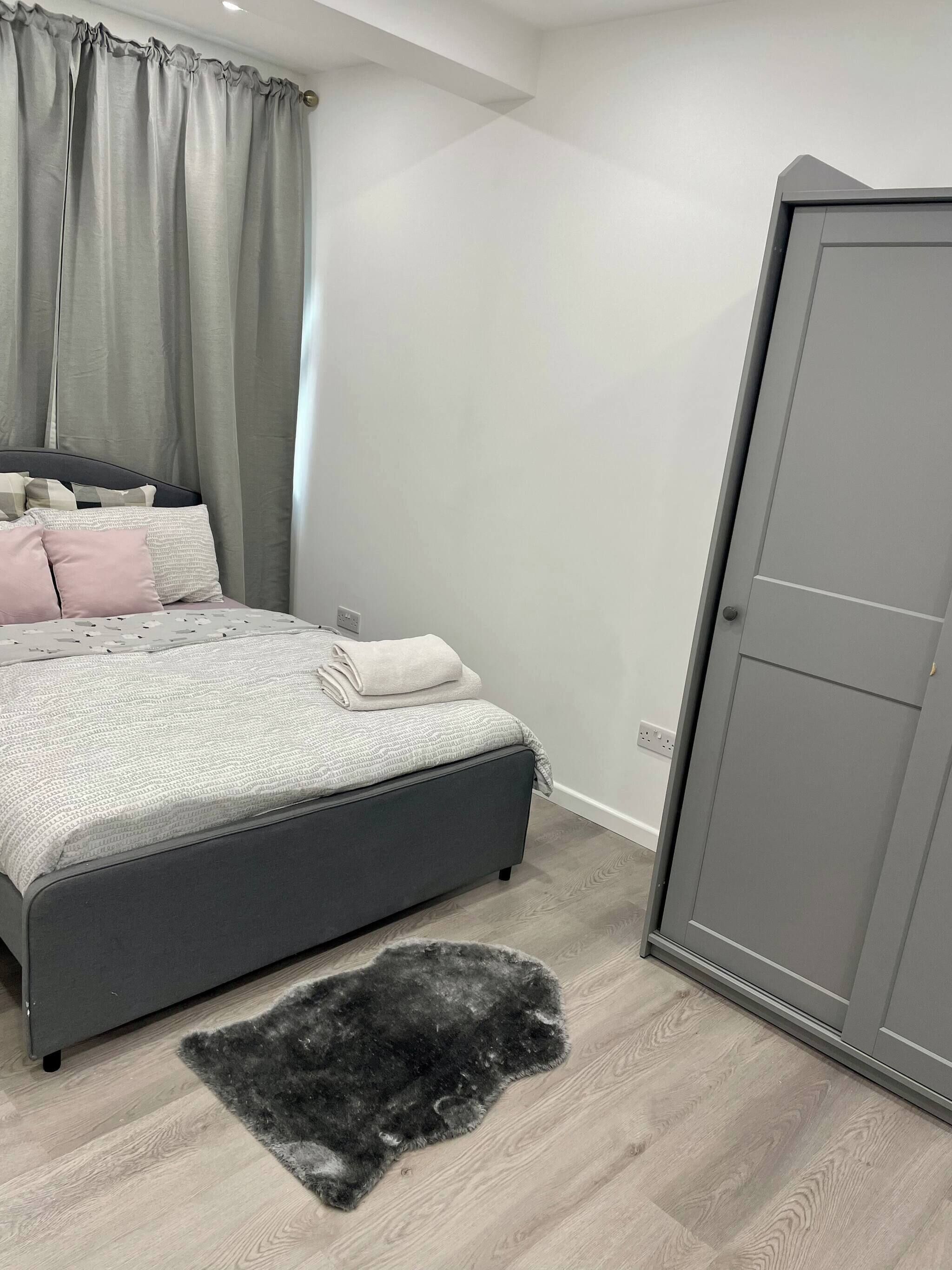 A bedroom with a bed, grey curtains, a grey wardrobe, and a black furry rug.
