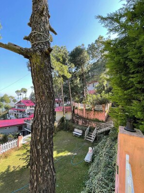 A residential area with a large tree, a grassy yard, a bench, and a staircase leading to a house with a red roof.