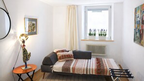A bedroom with a bed, a side table, a lamp, a radiator, and a window with a view of plants. - Dengg down town studios Apartment (Innsbruck)