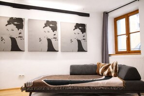 Una habitación con un sofá gris, una manta con estampado y tres cuadros en blanco y negro en la pared.