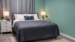 Quarto com cama, mesas de cabeceira, tapete e luminária no teto.