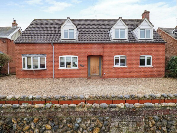 A red brick house with a tiled roof, a wooden door, and multiple windows. - Cliff Cottage (Norwich)