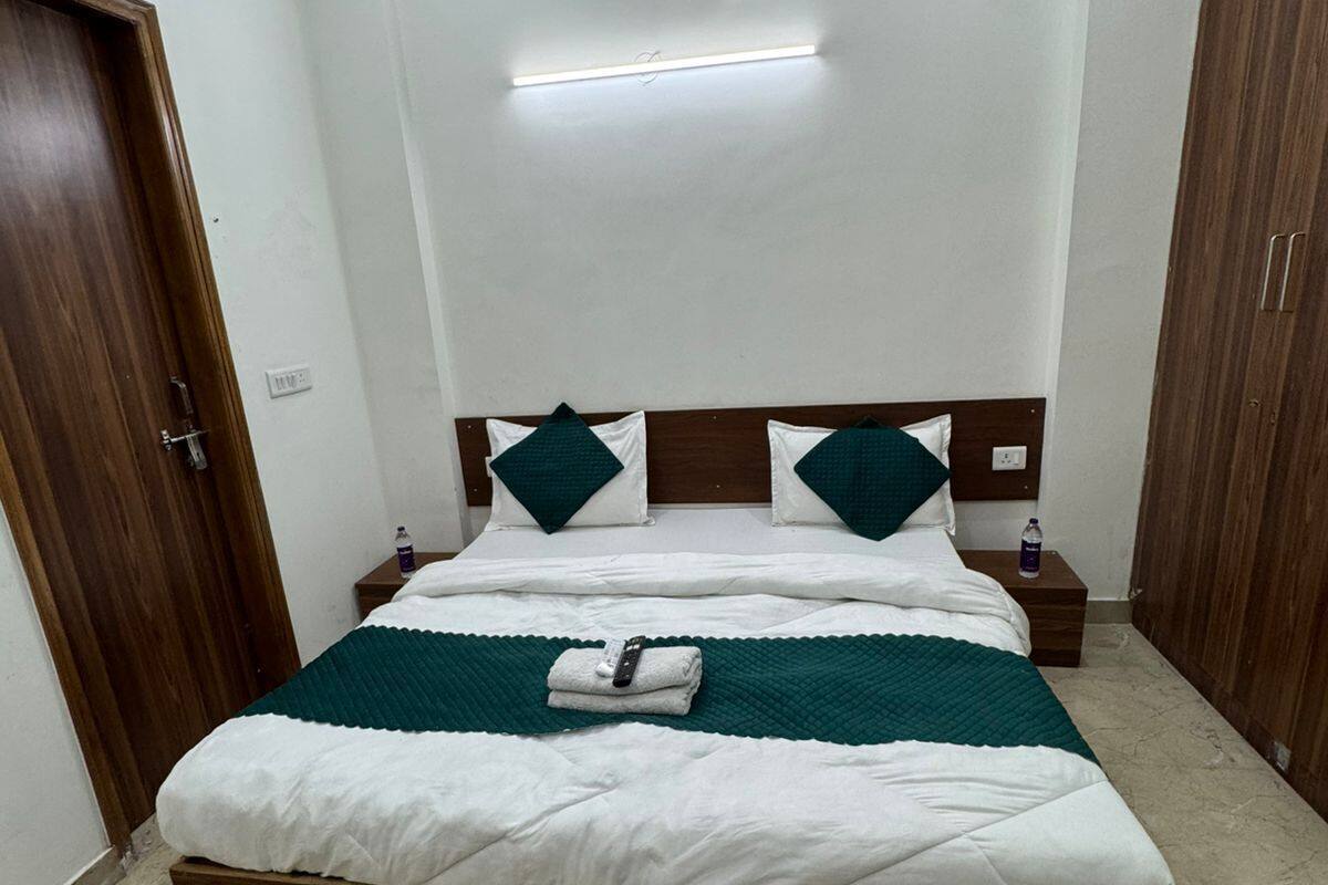 Ein ordentlich bezogenes Bett mit Holz-Kopfteil, ein Nachttisch mit einer Flasche und ein Beistelltisch mit einer Lampe.