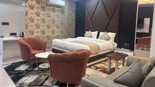 A modern hotel room with a large bed, two armchairs, a sofa, a small table, and a desk. - Hotel Rashmi Grand (Khagaria)