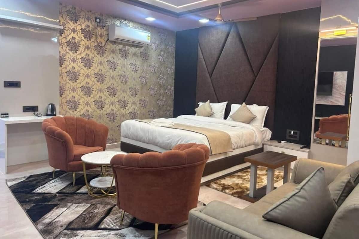 Una habitación de hotel moderna con una cama grande, dos sillones, un sofá, una mesita y un escritorio.