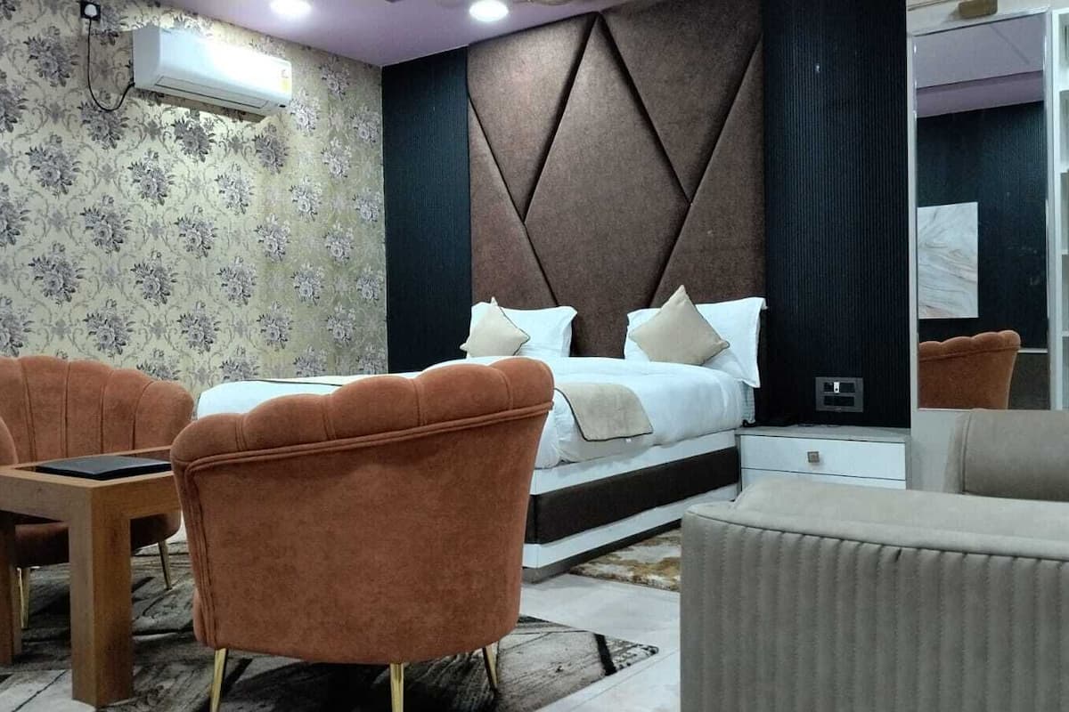 Un dormitorio con una cama, dos sillones, una mesita, una mesilla de noche y un espejo.