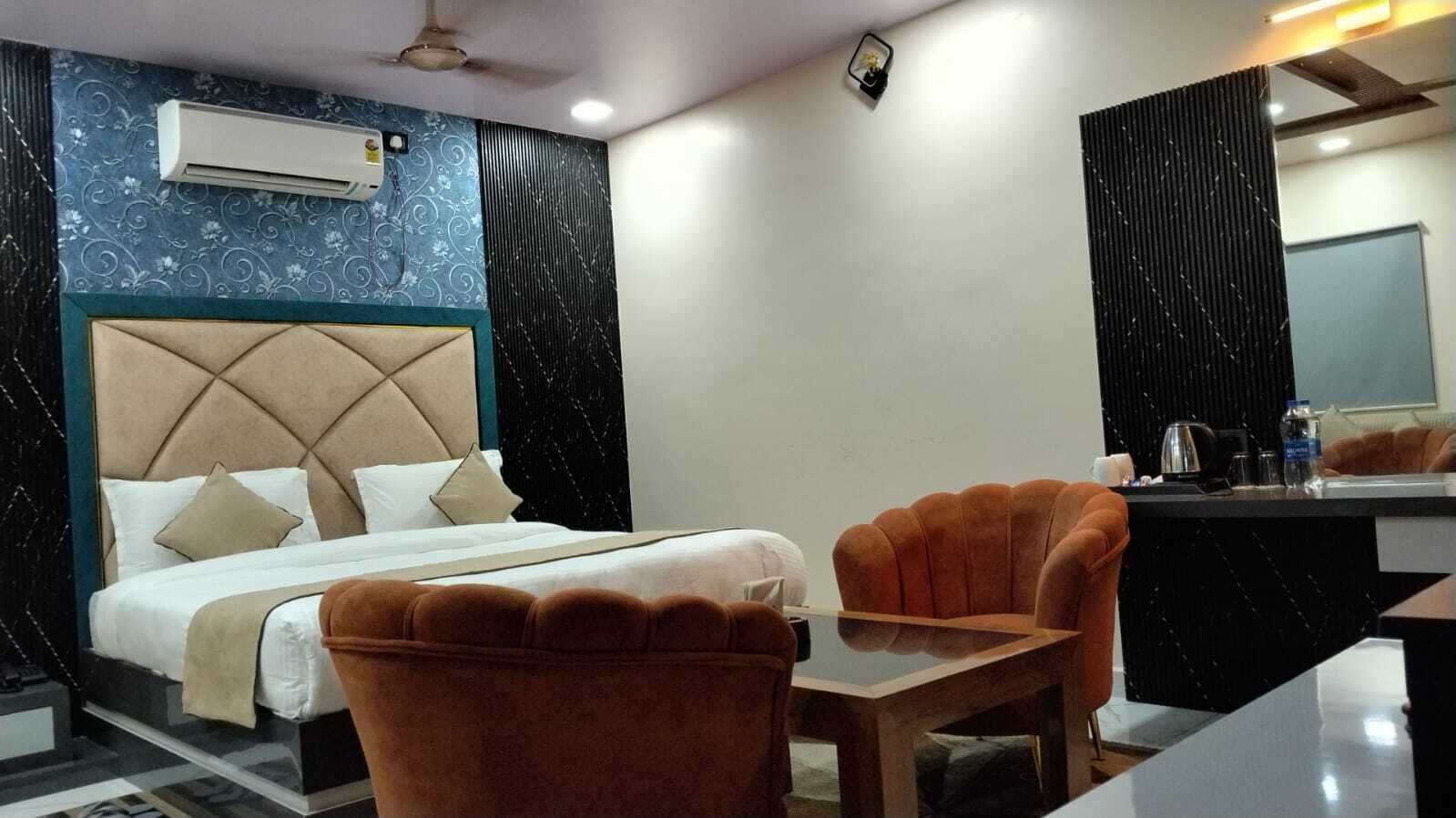 A hotel room with a bed, two armchairs, a small table, a mirror, and a wall-mounted air conditioner.