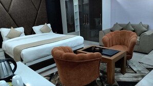 A modern hotel room with a bed, two armchairs, a coffee table, and a minibar. - Hotel Rashmi Grand (Khagaria)