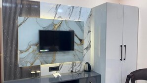 A modern room with a marble wall, a flat-screen TV, a coffee maker, and a wardrobe. - Hotel Rashmi Grand (Khagaria)