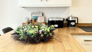 A wooden table with a floral centerpiece, a coffee maker, and a kettle on a kitchen counter. - The Ravens Inn, 4 - Bed, Sleeps 6, Long Term Rental Available (Ulverston)