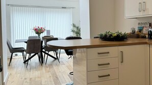 A modern kitchen with white cabinets, a wooden countertop, and a dining area with a table and chairs. - The Ravens Inn, 4 - Bed, Sleeps 6, Long Term Rental Available (Ulverston)
