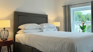 A neatly made bed with white linens, a grey upholstered headboard, and two bedside lamps. - The Ravens Inn, 4 - Bed, Sleeps 6, Long Term Rental Available (Ulverston)