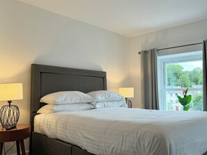 A neatly made bed with white linens, a grey upholstered headboard, and two bedside lamps. - The Ravens Inn, 4 - Bed, Sleeps 6, Long Term Rental Available (Ulverston)