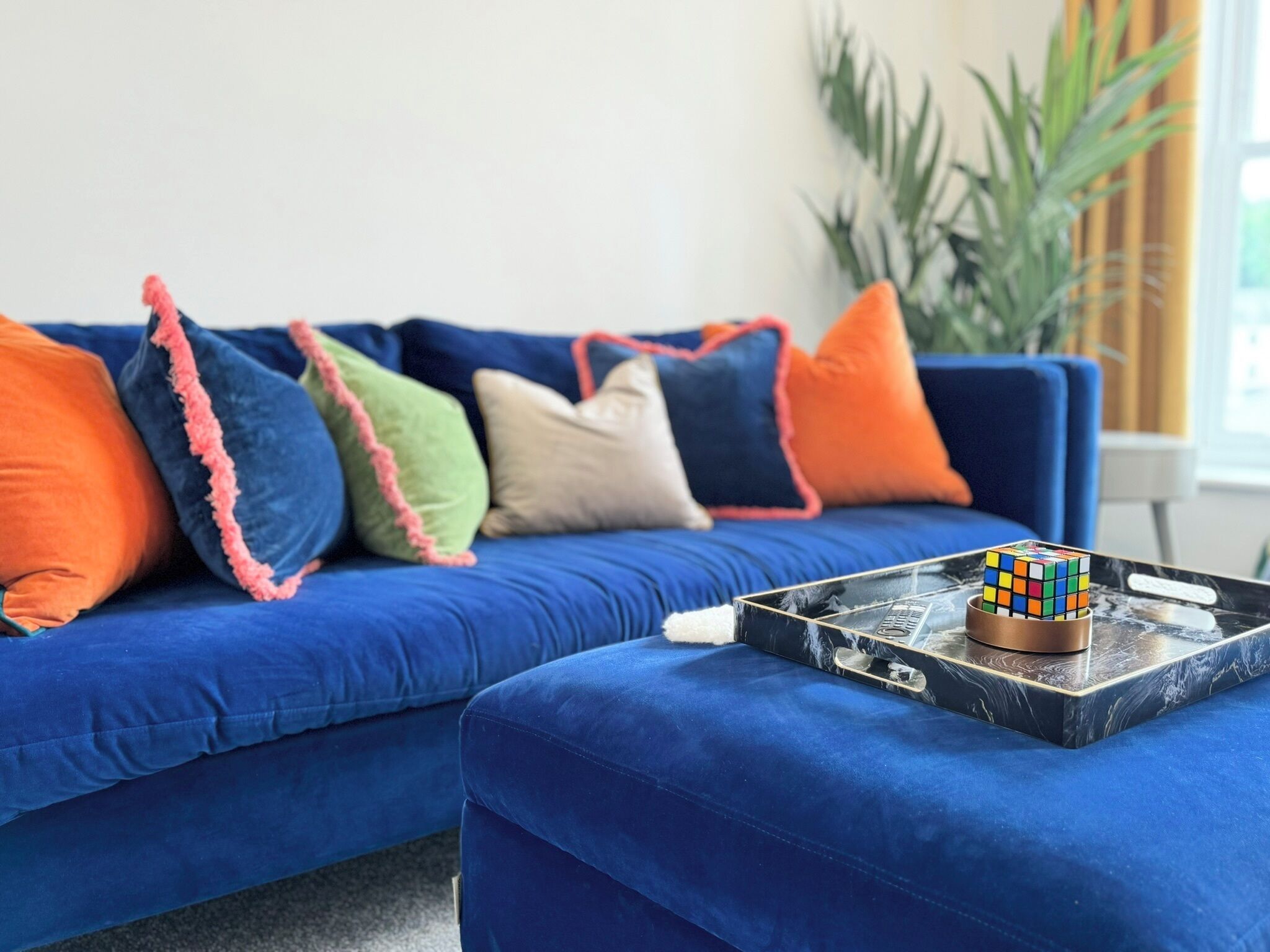 A blue sofa with colorful pillows and a Rubik's Cube on a marble tray.
